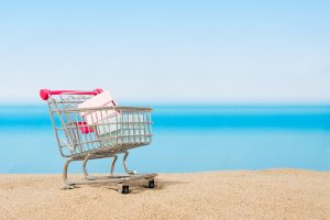 A miniature shopping cart sitting on the beach with some tiny boxes inside