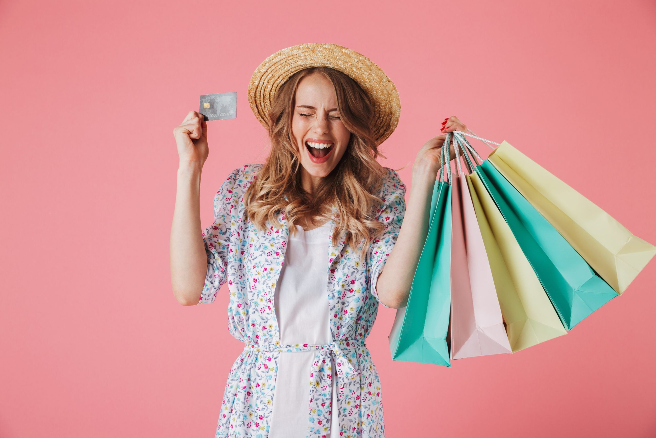 A woman dressed for summer, happily carrying shopping bags in one hand and her credit card in another