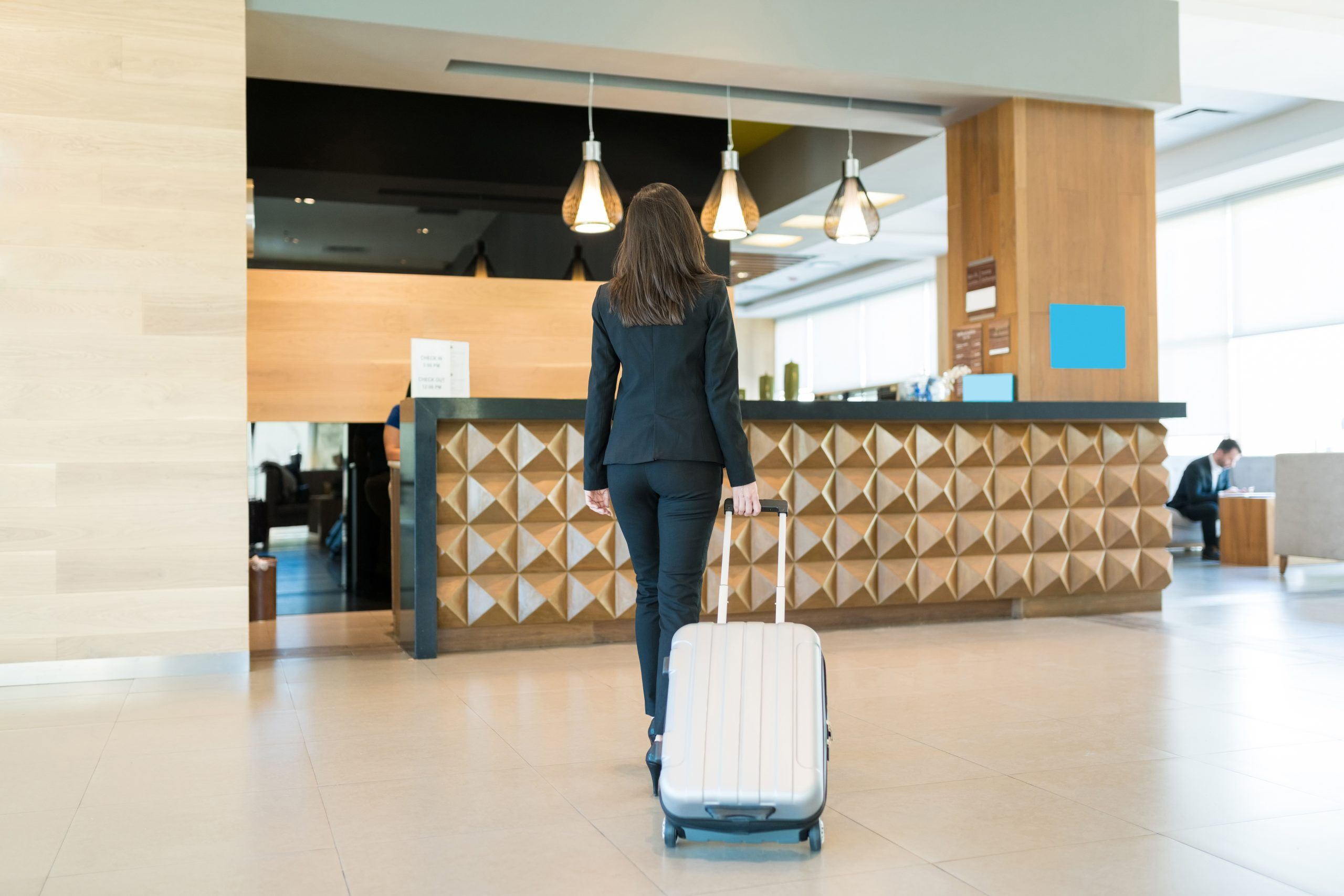 A woman in a suit pulling a silver suitecase as she walks up to a gold-decorated hotel lobby