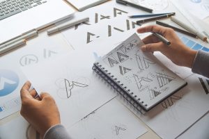 A designer holding some notebooks and papers with several variations of a logo design for a stylized letter A.