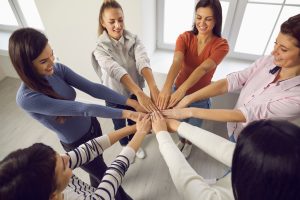 A top view of a diverse group of women standing in a circle, holding out their hands to the center as a sign of teamwork and camaraderie.