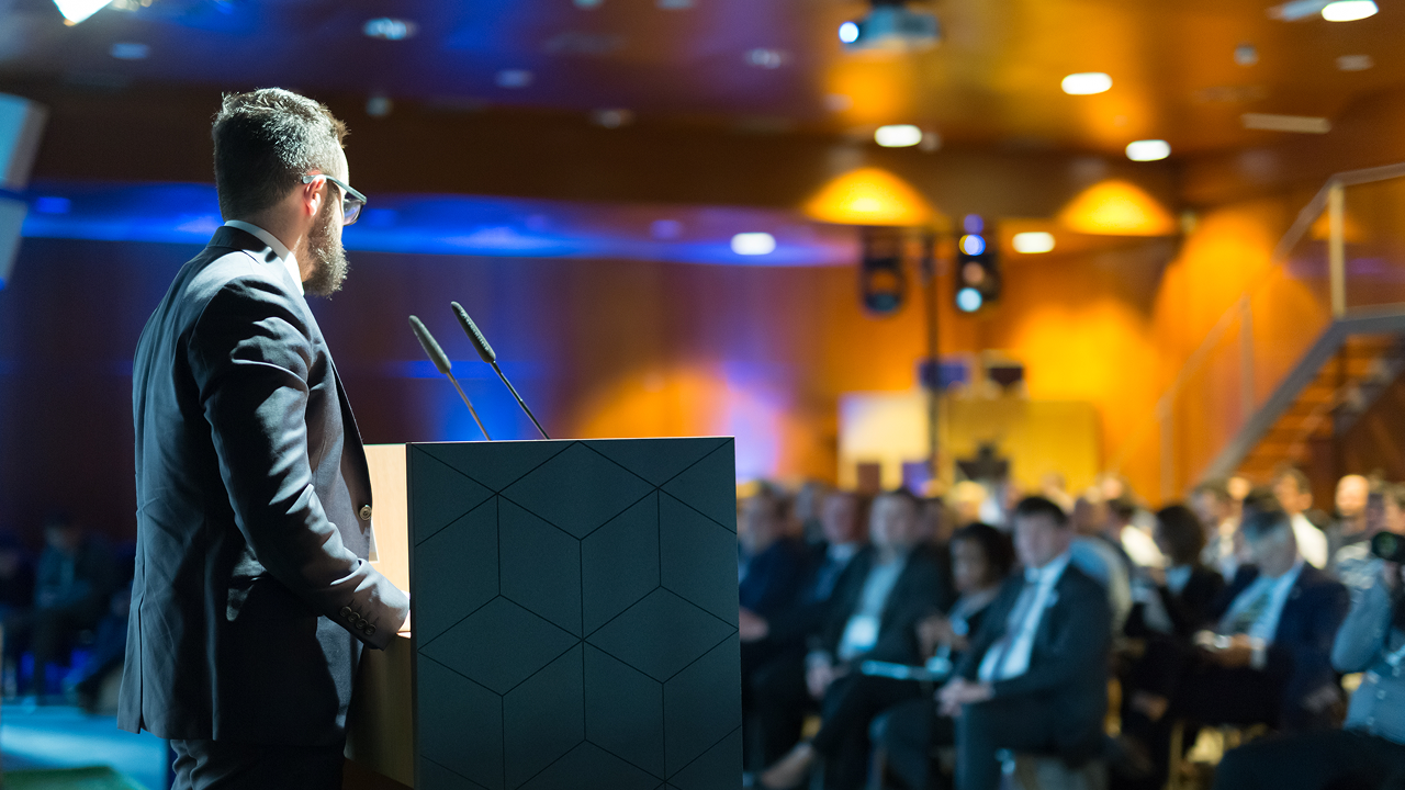 man in a suit standing on a podium in front of a crowd